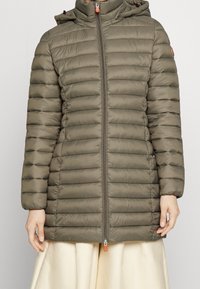 Parka matelassée en vert olive, avec des sections matelassées horizontales, une capuche, une fermeture éclair à l'avant avec un tirant orange, et des poignets élastiques.