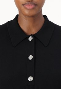 Polo nero con colletto, dotato di quattro bottoni in argento e una texture a coste. Vista ravvicinata dei bottoni e del colletto.
