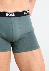 Zöld pamut boxer alsónadrág fekete derékkal, amelyen fehér "BOSS" logó található. Az anyag sima, és illeszkedő kialakítású.