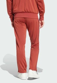 Pantalons de sport bordeaux en tissu lisse, dotés d'une taille élastique, de chevilles fuselées et de rayures sur les côtés. Associés à des baskets blanches.