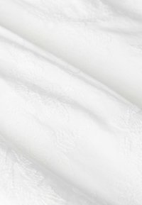 White fabric with an embossed floral pattern. The texture is soft and smooth, featuring subtly raised designs. Subtle sheen visible.