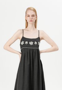 Abito senza maniche nero con ricami floreali bianchi, busto arricciato e gonna fluida. Realizzato in un tessuto leggero.