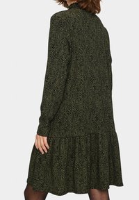 Långärmad klänning i mörkgrön med ett zigzag-mönster. Lagerdesign, tillverkad av texturerat material. Halvlång, avslappnad passform.