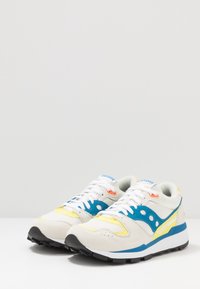 Vita sneakers med blå accenter och gula detaljer. Ovandel i mesh med mockainslag, med en svart gummisula och snörning fram.