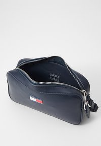 Tamno plava kožna toaletna torbica s zatvaranjem na zatvarač, srebrnim hardverom i logotipom Tommy Jeans. Glatka tekstura s pravokutnim oblikom i suptilnim šavovima.