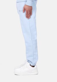 Light blue sweatpants with ribbed cuffs, featuring a side pocket and embroidered text. Paired with chunky white sneakers.