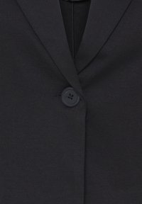Blazer noir avec un seul bouton sombre fermé, avec des revers crantés et une texture de tissu lisse.