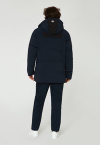 Marinblå puffjacka med svart huva och axelpanel, med en texturerad yta och subtil sömdetalj. Lämplig för kallt väder.