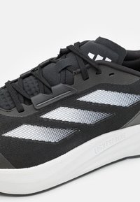 Scarpa sportiva nera con tomaia in maglia e dettagli in rete bianca, dotata di un tallone nero texturizzato. Ammortizzazione Lightstrike visibile sulla suola.