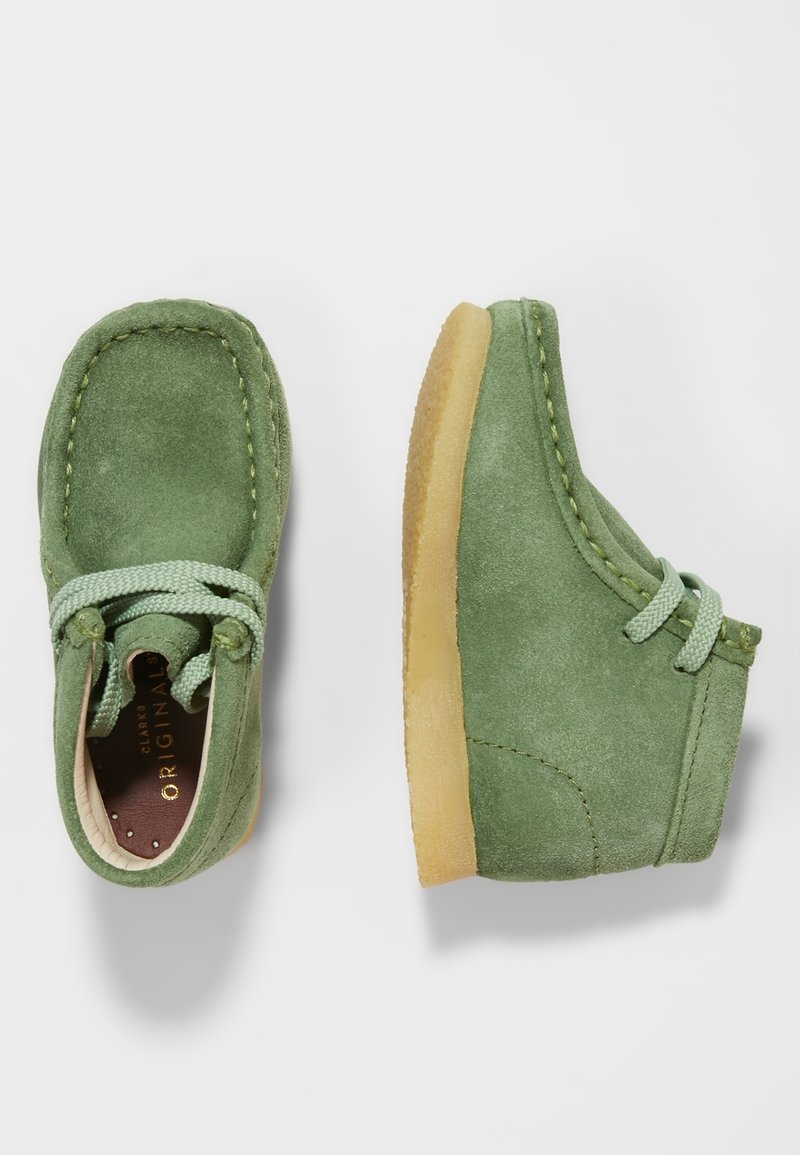 Paire de chaussures en daim vert pour tout-petits avec des lacets vert clair et des semelles en caoutchouc crêpé, montrées vues de dessus et de côté sur fond blanc.