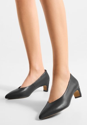 Décolleté nere in pelle con punta appuntita e tacco basso a blocco. Presentano un design con tagli sui lati e dettagli testurizzati sul tacco.