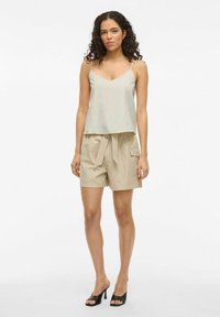 Top grigio chiaro senza maniche con scollo a V, abbinato a pantaloni beige con vita a sacchetto e tasche laterali. Tacchi neri open-toe.