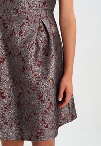 Burgundská šaty s stříbrnou květinovou výšivkou, přiléhavá korzet, rozšířená sukně, boční záhyb a texturovaná látka.