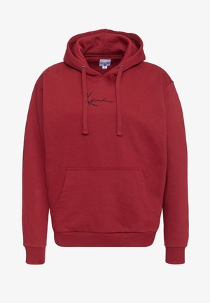 Punane puhvri, mis on valmistatud puuvillast, esiküljel tasku, reguleeritava kapuutsiga ja musta nõelteksti kätkeb rinnal. Pehme tekstuur.