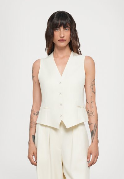 Gilet sans manches blanc avec un décolleté en V, comportant six boutons sur le devant, des poches latérales discrètes et une coupe ajustée. Texture lisse.