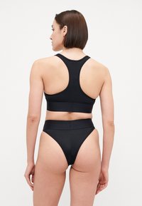 Fekete sportmelltartó, versenyháttal, magas derekú fekete bikini alsókkal párosítva. Sima textúra, minimális varrások, és nincs látható hardver.