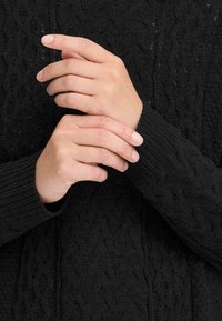 Mustmust sokk, millel on tekstuuriga kaabeldisain ja soonilised varrukad, käed on rahulikus asendis, näidates kanga detaile.