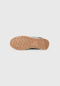 Black athletic shoe with a textured rubber sole featuring a diamond pattern, contrasting lighter brown traction grips for stability.
