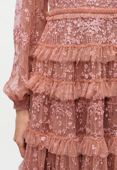 Ροζ δαντελένιο φόρεμα με κεντήματα λουλουδιών και στρωμένες λεπτομέρειες βολάν στο μανίκι και τη μέση, φορεμένο στο κάτω μέρος του κορμού και στο χέρι.