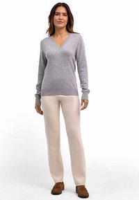 Lichtgrijze v-hals trui met geribbelde manchetten en zoom, gecombineerd met crèmekleurige rechte broek en bruine instapschoenen.
