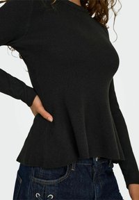 Haut noir à manches longues et à nervures, avec un ourlet évasé et un col rond, associé à un jean en denim foncé avec des coutures de poches visibles.