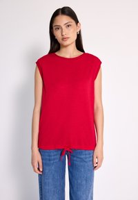 Top rojo de manga corta con cuello redondo, que cuenta con un dobladillo con cordón recogido y una tela suave y ligera. Combinado con pantalones de mezclilla azul.