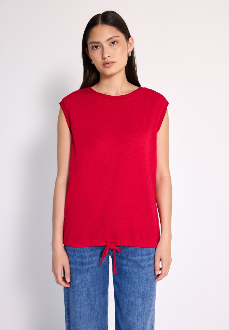Top rojo de manga corta con cuello redondo, que cuenta con un dobladillo con cordón recogido y una tela suave y ligera. Combinado con pantalones de mezclilla azul.