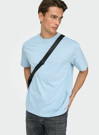 Light blue short-sleeve t-shirt made of cotton, featuring a round neckline, relaxed fit, and smooth texture, worn with dark jeans and a black strap bag.