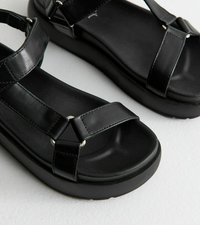 Svarta sandaler med en slät läderöverdel, platt sula och korskorsade remmar med metalliska detaljer för säker passform.