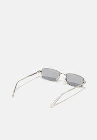 Lunettes de soleil métallic argent avec des verres rectangulaires gris. Les caractéristiques incluent des branches fines et des accents en plastique transparent sur les plaquettes de nez.