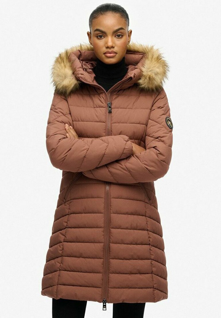 Beżowy płaszcz pikowany z kapturem wykończonym futrem, z zamkiem błyskawicznym z przodu i poziomymi wzorami przeszyć, sięgający do połowy uda.