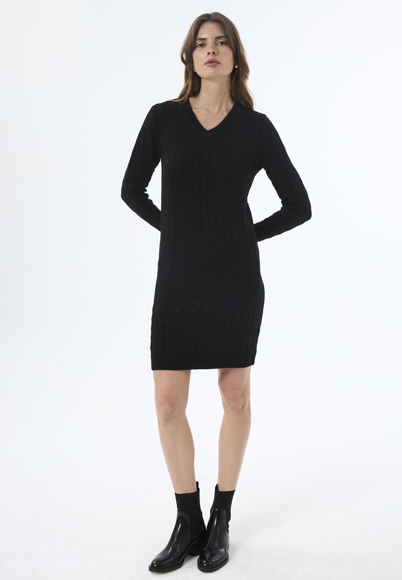 Must mustriga kleit V-kaelusega, pikkade varrukatega ja nöörmustriga, ulatudes reie keskele. Kombineeritud pahkluu kõrguste mustade saapadega.