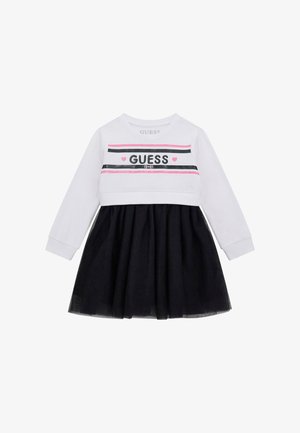 Robe à manches longues avec un haut blanc à rayures noires et roses et le texte "GUESS", associée à une jupe en tulle noire.