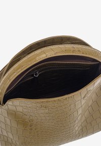 Zielona torebka z tłoczeniem imitującym skórę krokodyla, z kieszenią na zamek, ukazująca miękką wyściółkę i uporządkowany kształt. Charakteryzuje się zakrzywionym otwarciem.