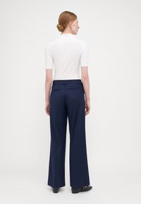 Navy wijde broek met een gestructureerde stof en twee achterzakken, gecombineerd met een witte top met korte mouwen. Neutrale achtergrond.