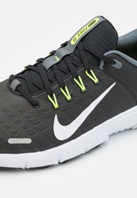 Čierna atletická obuv s textúrovaným zvrškom, bielym logom swoosh, zelenými akcentmi na šnúrkach a bielou podrážkou s kontrastnými čiernymi detailmi.