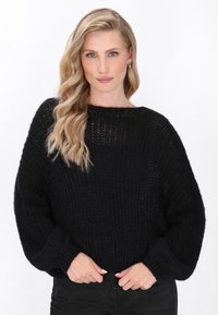 Pulover negru tricotat cu o croială lejeră, decolteu larg și mâneci lungi. Materialul texturat și manșetele ribbate oferă detalii. Combinație cu pantaloni negri.