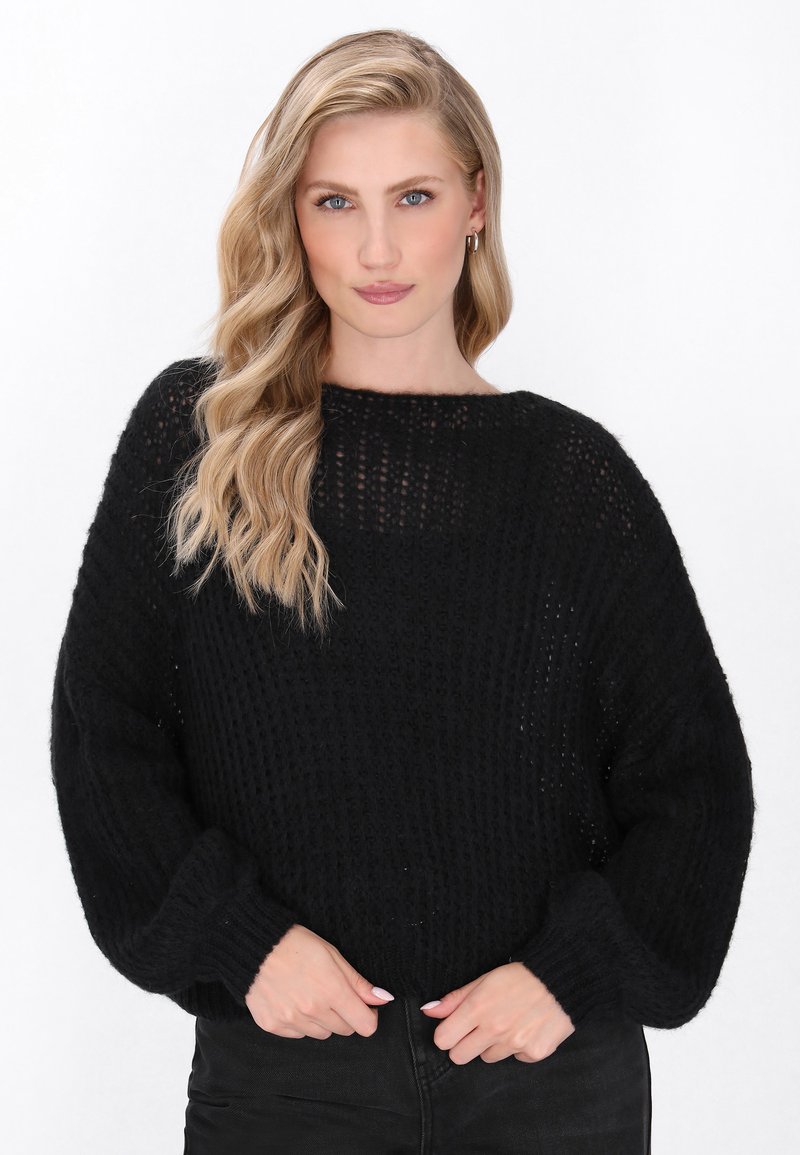 Pulover negru tricotat cu o croială lejeră, decolteu larg și mâneci lungi. Materialul texturat și manșetele ribbate oferă detalii. Combinație cu pantaloni negri.