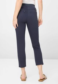 Pantaloni tapered in tessuto elasticizzato navy con una ampia vita elastica, due tasche posteriori e lunghezza cropped, abbinati a sandali piatti.