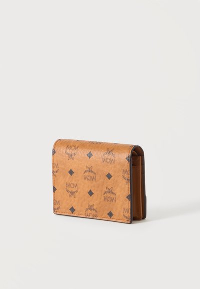 Portefeuille en cuir marron avec impression du logo MCM noir et formes losanges, debout sur un fond clair uni.