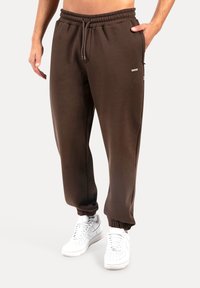 Brązowe bawełniane spodnie dresowe z elastycznym pasem, zwężanymi mankietami, bocznymi kieszeniami i małym logo z przodu. W połączeniu z białymi trampkami.