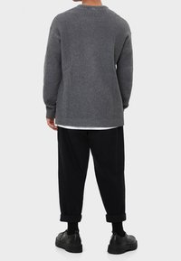 Grauer, gerippter Pullover mit rundem Ausschnitt und langen Ärmeln. Über einem weißen Hemd getragen und kombiniert mit schwarz zulaufenden Hosen und schwarzen Schuhen.