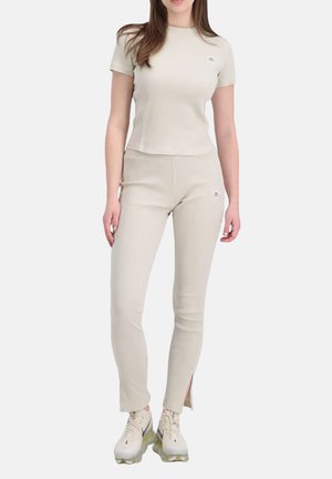 Beige ribbed t-shirt and matching pants, fitted design with side slits, paired with light-colored athletic shoes, minimal branding visible.