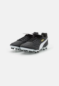 Botas de fútbol negras con una parte superior de cuero texturizado, acentos blancos y una suela de goma con tachuelas negras para tracción.