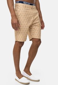 Pantalones cortos beige con un estampado de diamantes y una cinturilla azul marino con el logo "INDICODE". Fabricados con un tejido ligero.