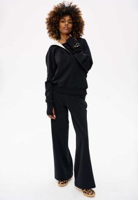 Zwarte relax-fit sweatshirt met een witte kraag, gecombineerd met zwarte wijde broek en flats met dierenprint. Zacht materiaal, losse pasvorm.