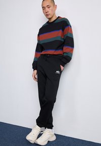 Sorte sweatpants med elastisk talje og sidelommer, parret med en langærmet stribet sweater i grøn, brun og blå. Hvide sneakers.