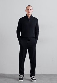 Black zip-up sweater with long sleeves, paired with matching black joggers and black sneakers. Smooth texture, casual fit, minimal design.
