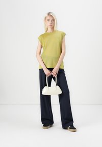 Lime green knitted top with cap sleeves, paired with navy wide-leg trousers and a small white handbag; model stands against a plain background.