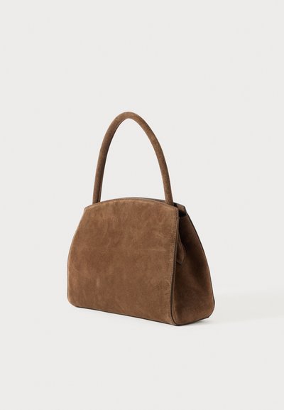 Καφέ σουέτ τσάντα με καμπύλη λαβή και δομημένο σχήμα τραπεζοειδούς, εκτεθειμένη σε λευκό φόντο.